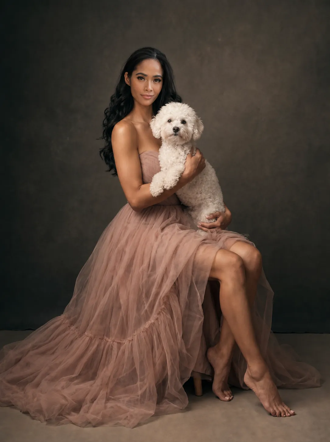 Woman in a blush tulle gown seated barefoot with her white dog against a dark painted backdrop